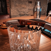 Wine opener resting on a glass tumbler on a wooden table, with a metal shaker in the background