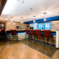 Modern bar interior with stone counter, red stools, and blue-lit windows