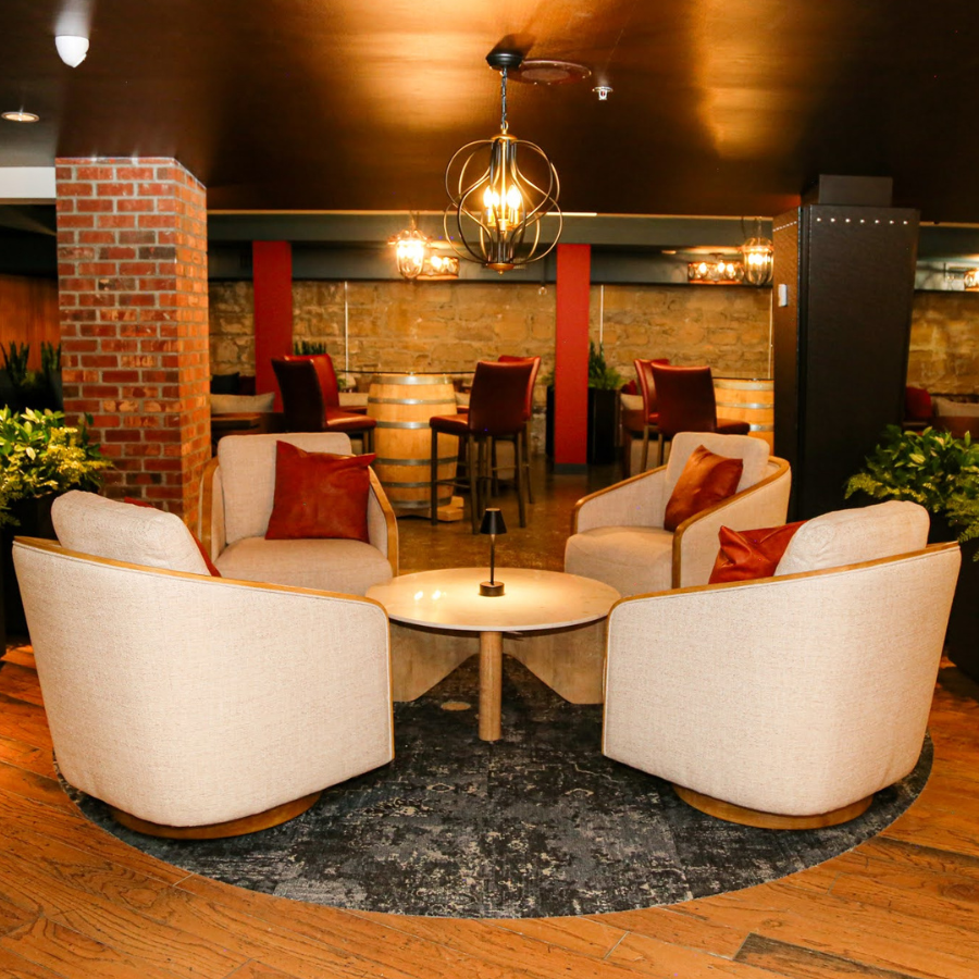 Cozy lounge with cream armchairs, red accents, bar stools, and warm pendant lighting