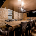 Modern rustic conference room with a long wooden table, leather chairs, stone walls, and a TV screen