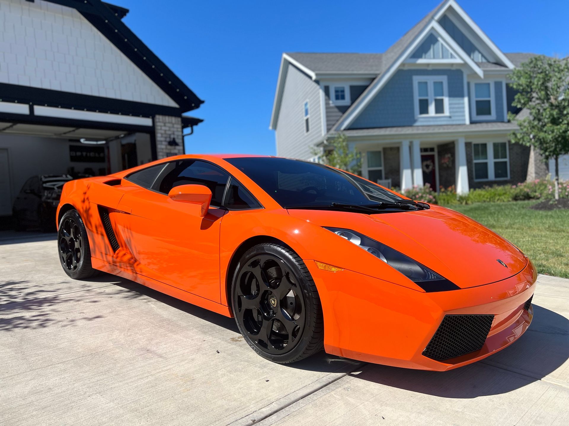 Bright orange Lamborghini parked on a driveway in front of a house.