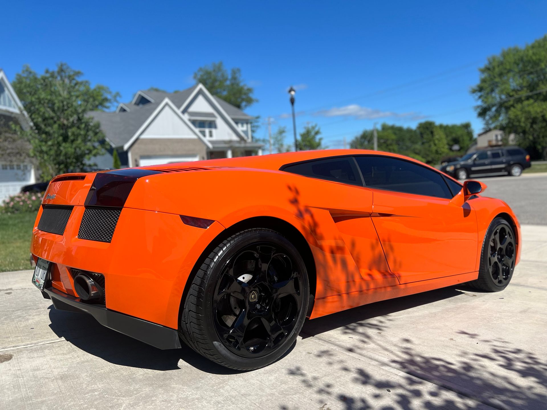 Orange Lamborghini sports car with black rims parked on a driveway, sunny day.