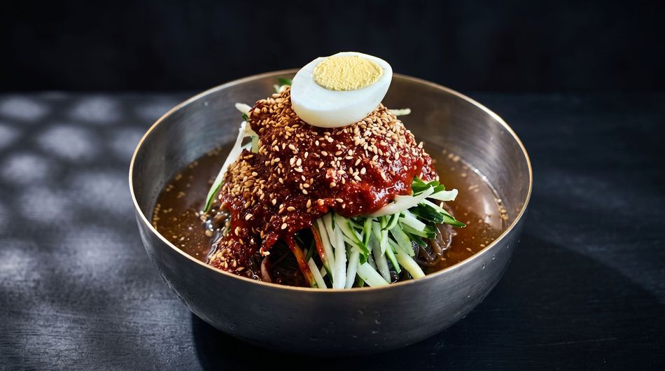 Korean cold noodle dish topped with sesame seeds and half a boiled egg in a metal bowl