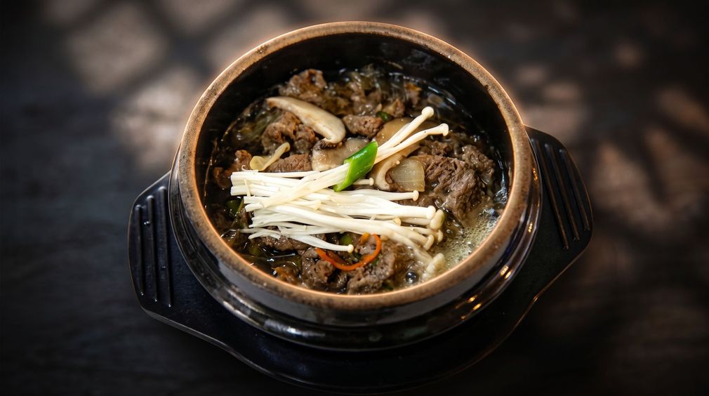 Korean stone pot soup topped with sliced mushrooms and green onions on a dark table