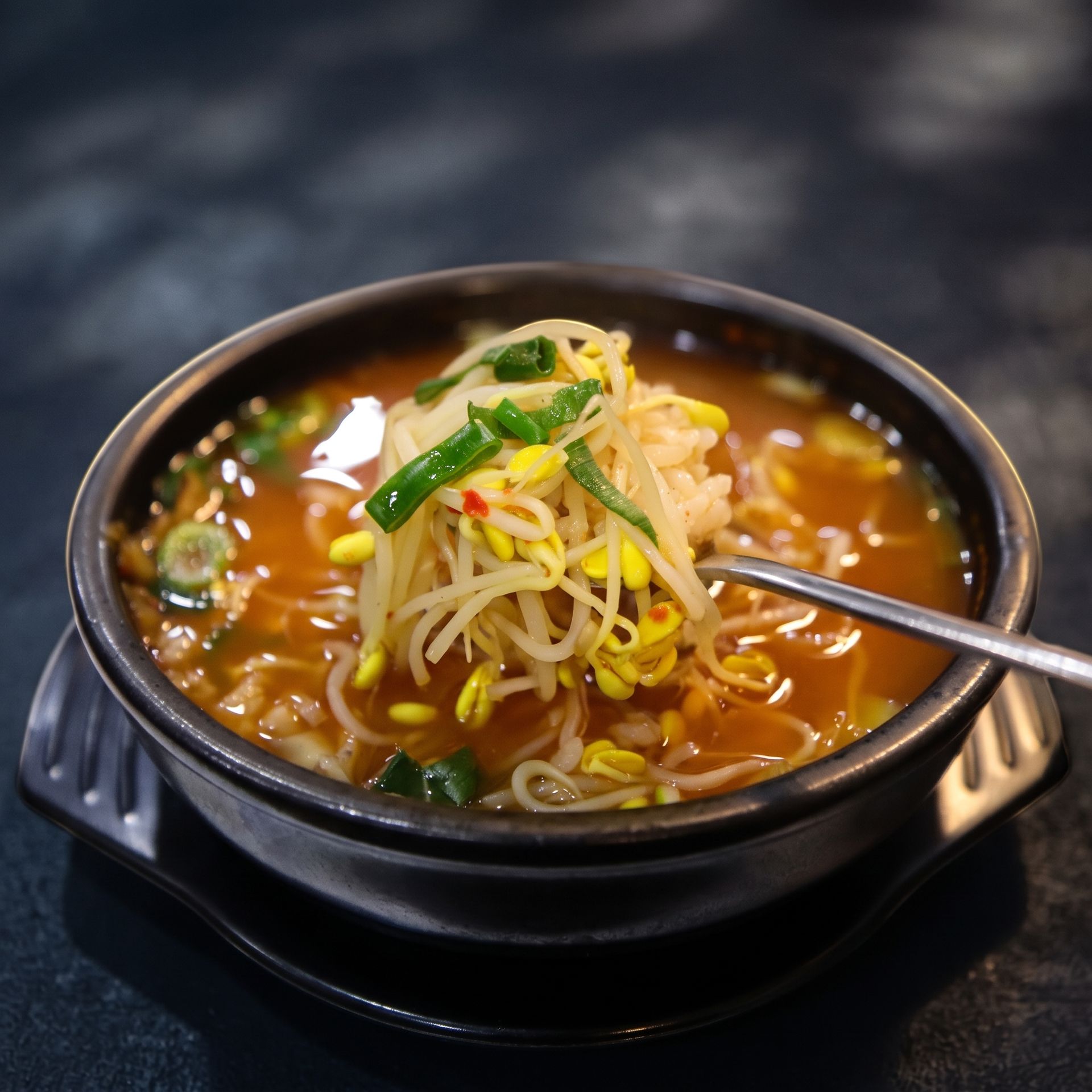 Bowl of spicy ramen topped with bean sprouts and green onions, with chopsticks lifting noodles