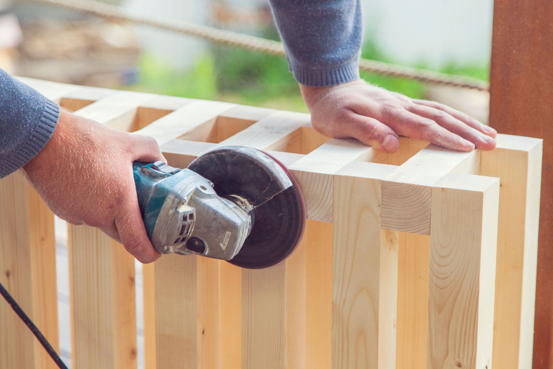 Hands using a power sander on a light wood crate frame