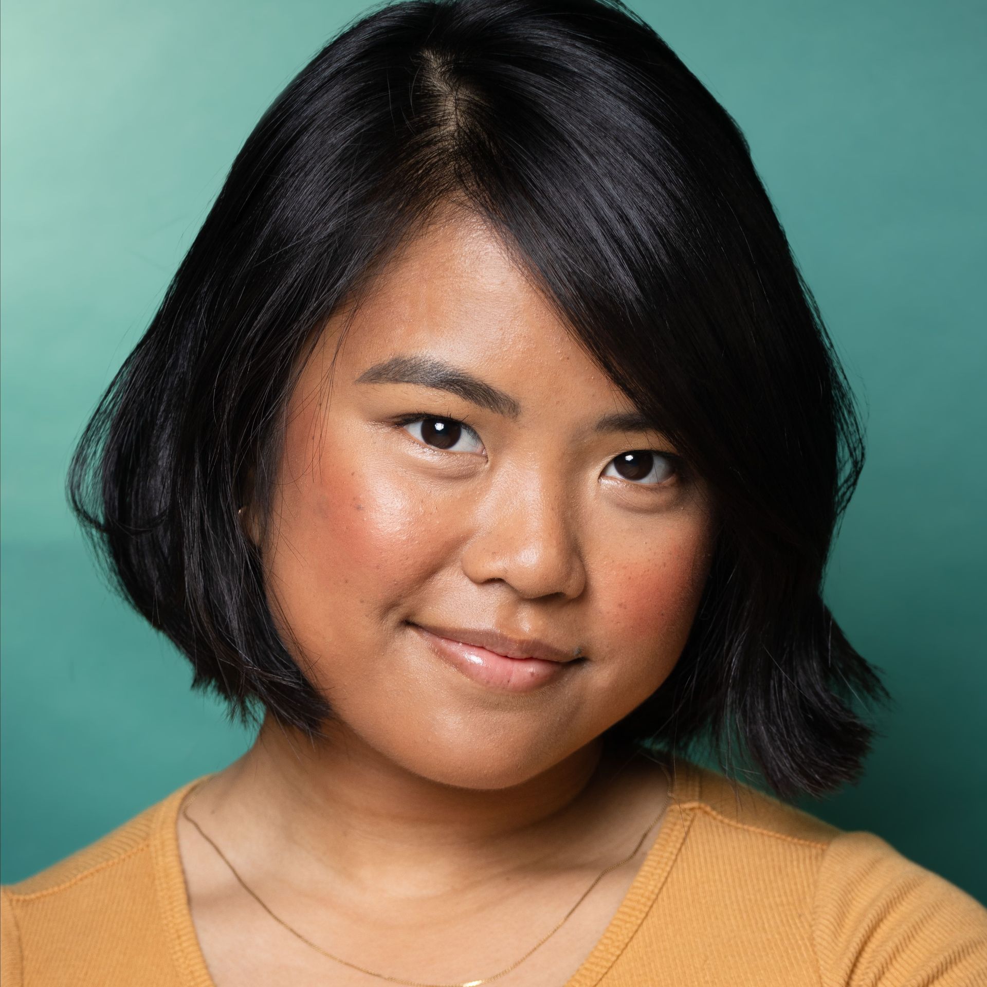 Portrait of a smiling person with short black hair against a teal background