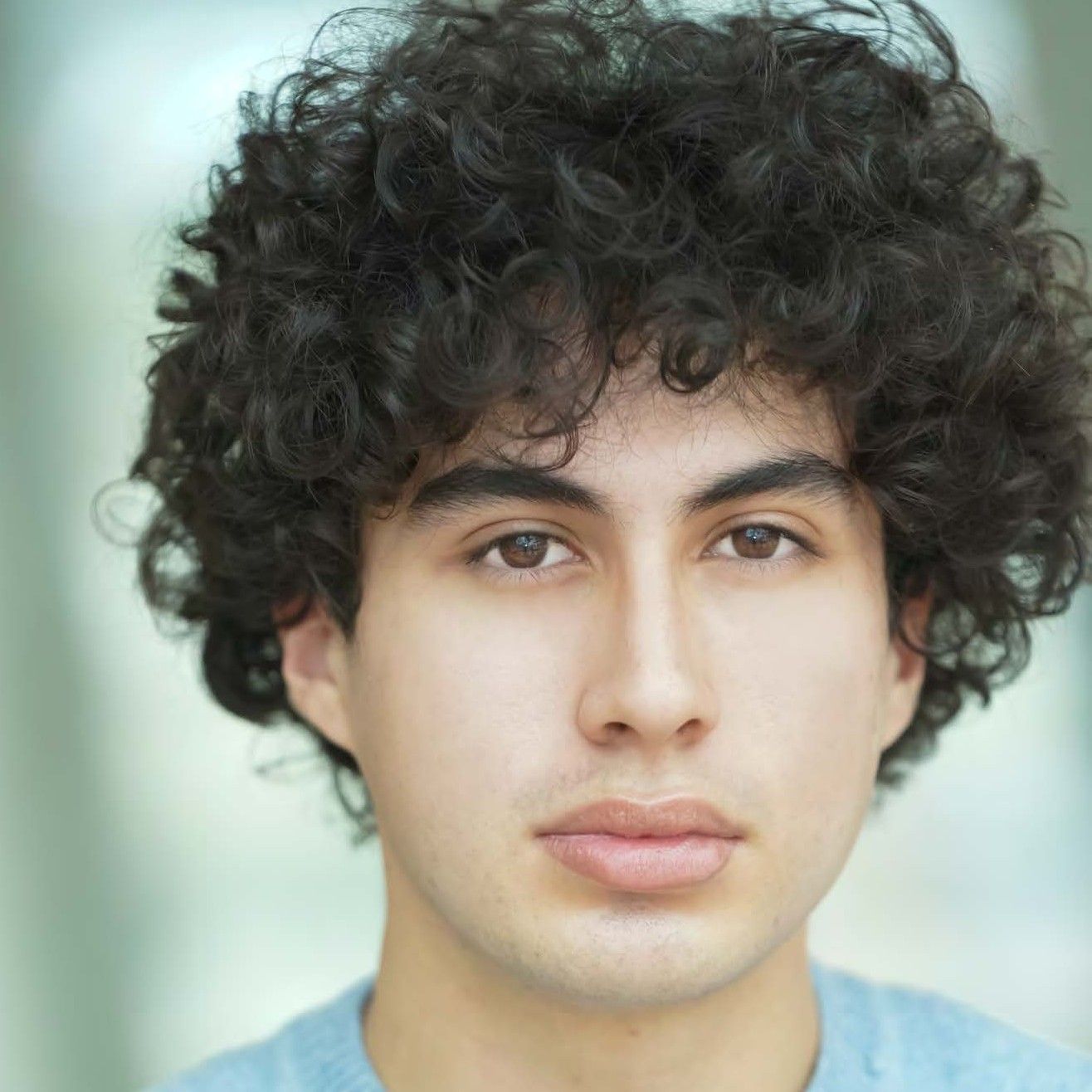 Close-up portrait of a person with curly dark hair against a soft green background.