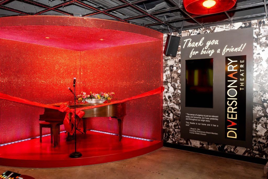 A red stage with a grand piano and microphone, next to a black sign with