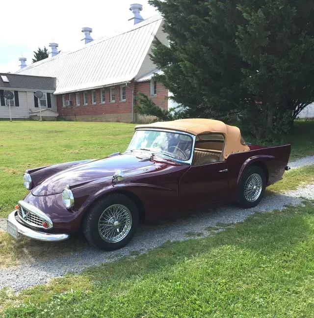 a burgundy sports car is parked in front of a barn