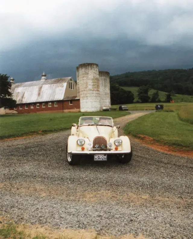 a car is parked on a gravel road with a barn in the background