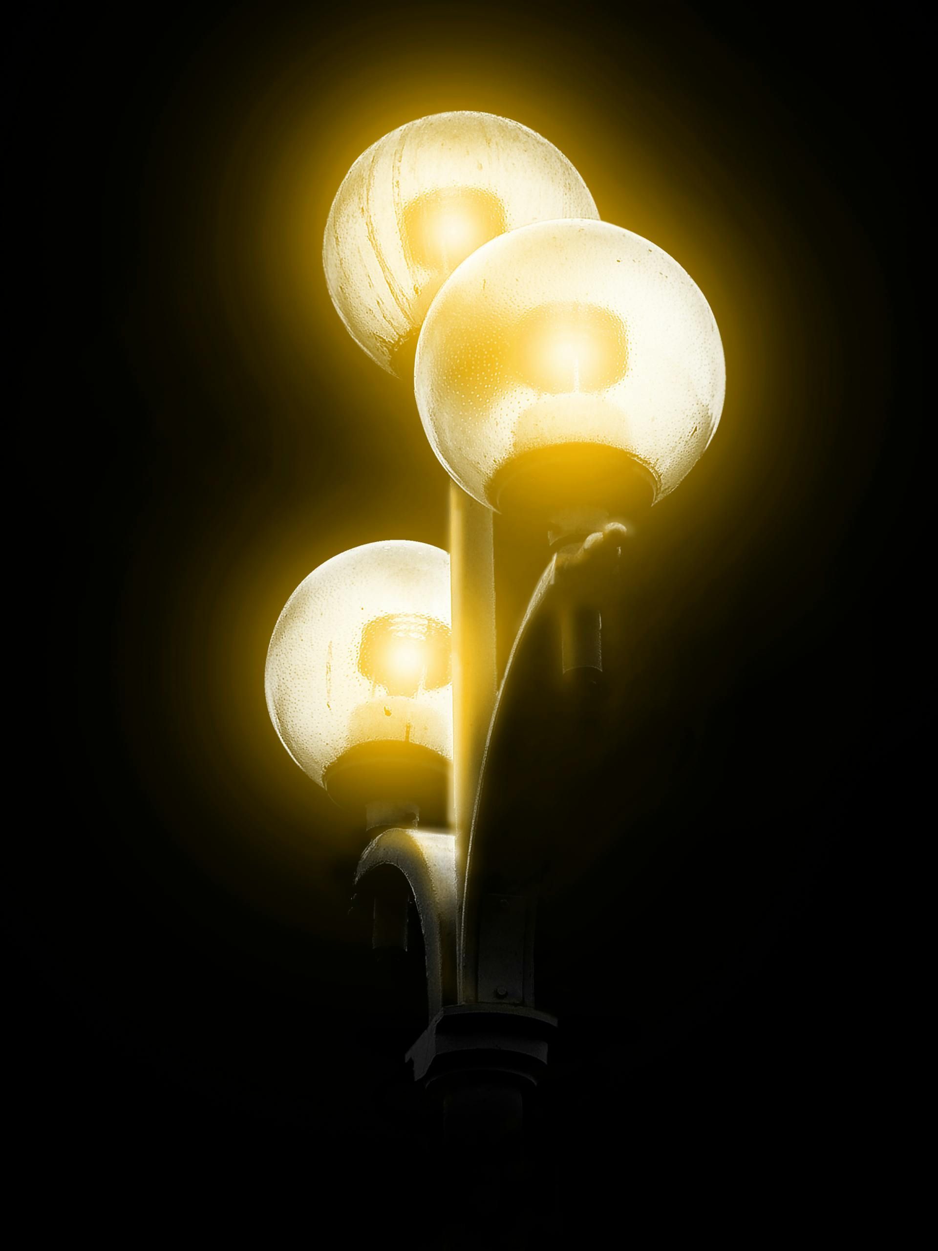 Trois lampadaires ronds et lumineux se détachent sur un fond sombre, émettant une lumière jaune chaude.