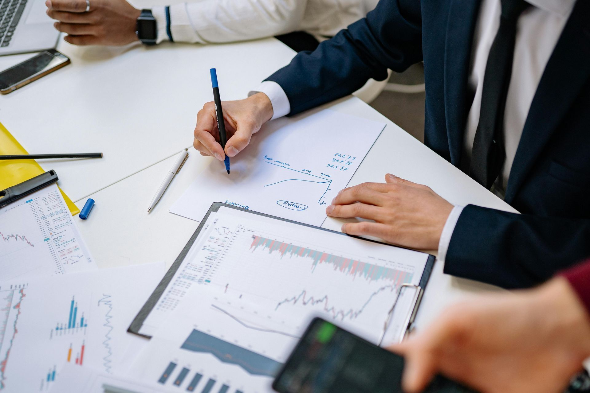 Des professionnels collaborent autour d'une table, examinant des graphiques et des données sur papier tout en discutant d'informations commerciales.