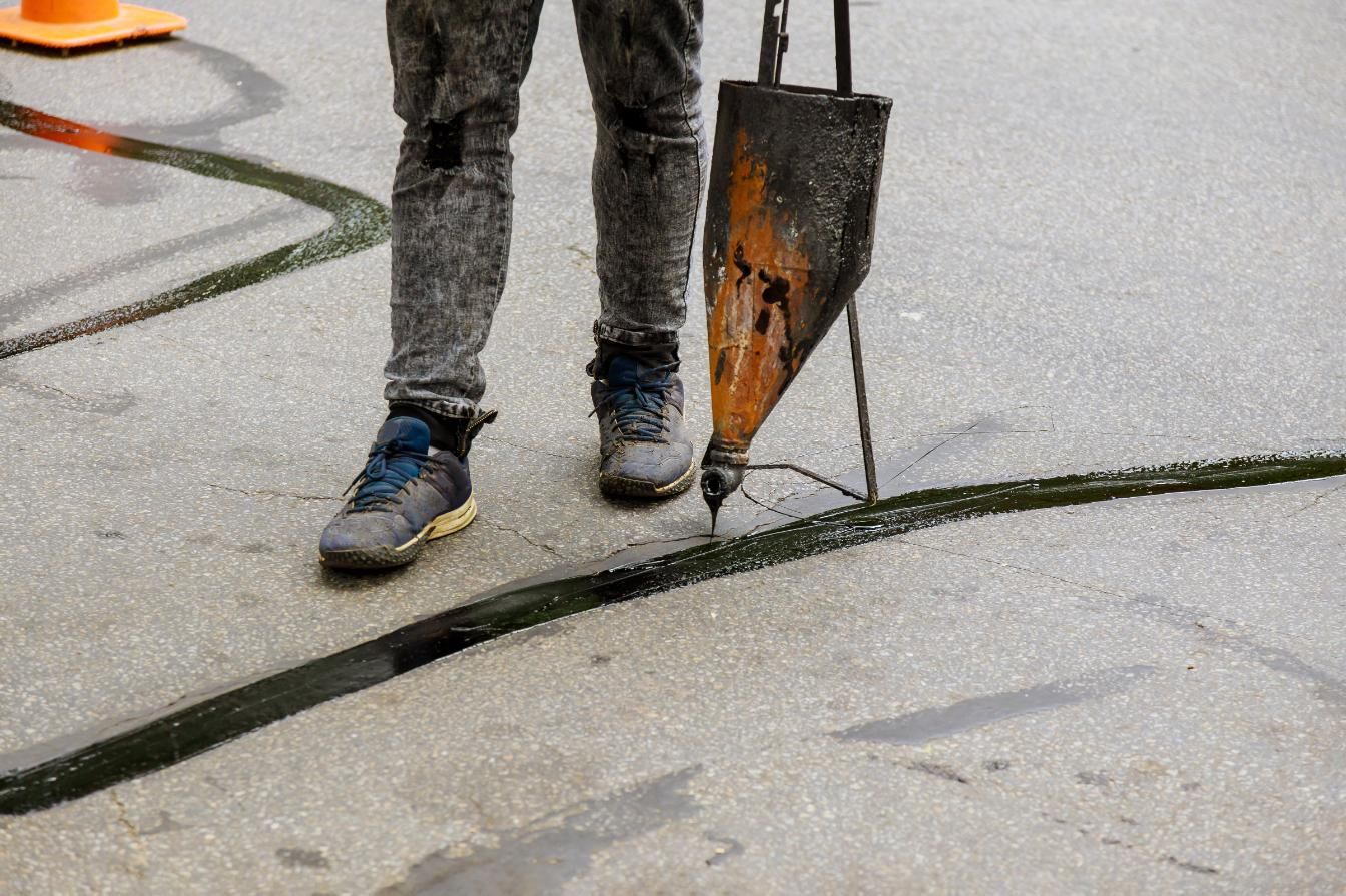 A person is standing on a sidewalk holding a tool.