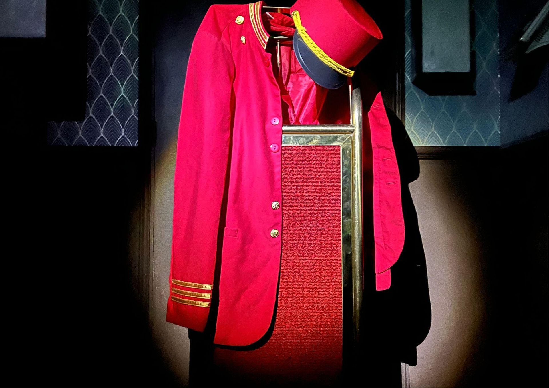 Une veste rouge et un chapeau haut de forme sont accrochés à un support.