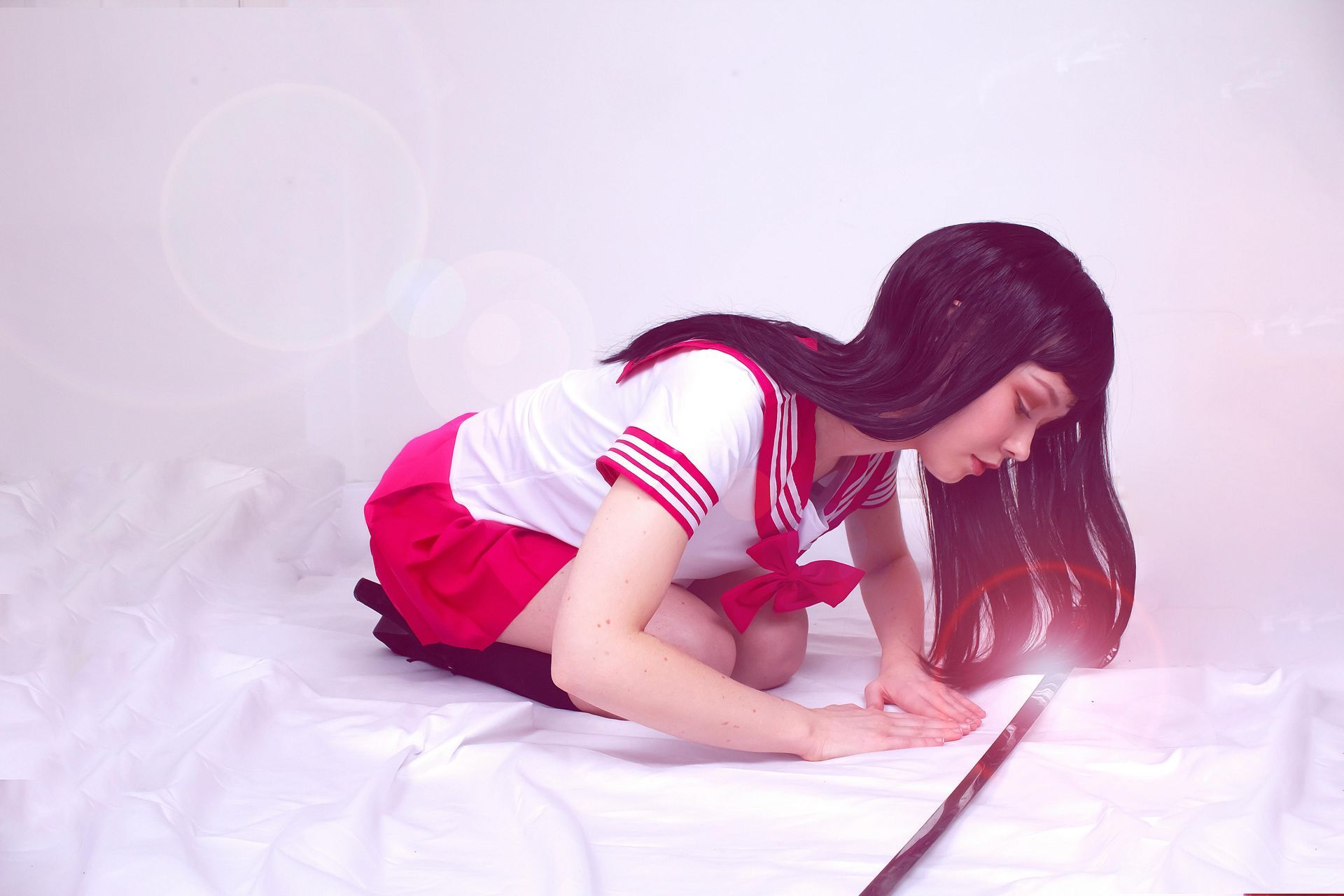 Femme agenouillée, regardant une baguette lumineuse posée sur un drap blanc, vêtue d'un uniforme scolaire rouge et blanc.