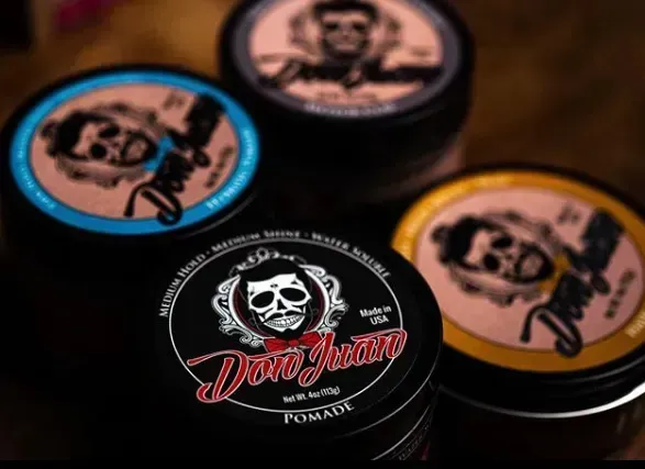 Cuatro latas redondas pequeñas con etiquetas con el logotipo de una calavera en negro, rosa, azul y amarillo sobre una superficie cálida.