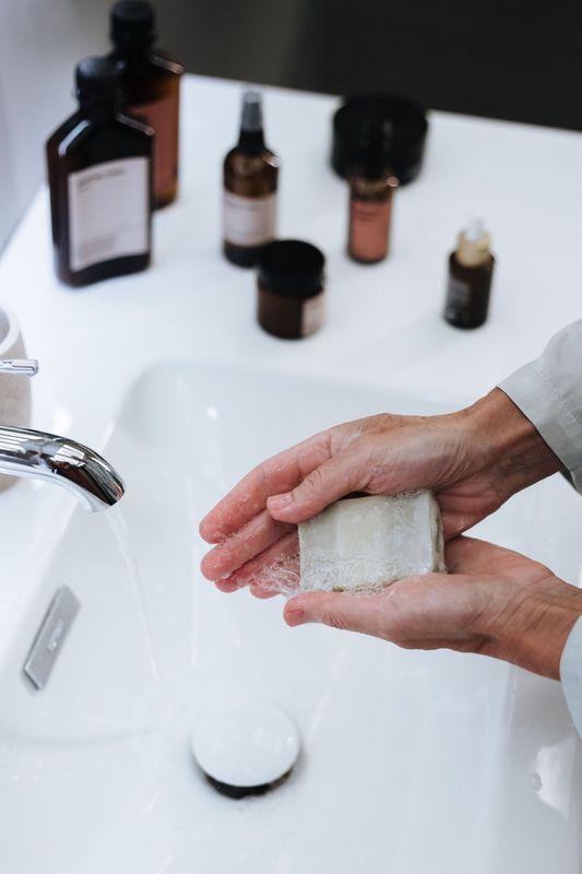 Lavado de manos con jabón en un lavabo blanco, con artículos de aseo personal sobre la encimera.