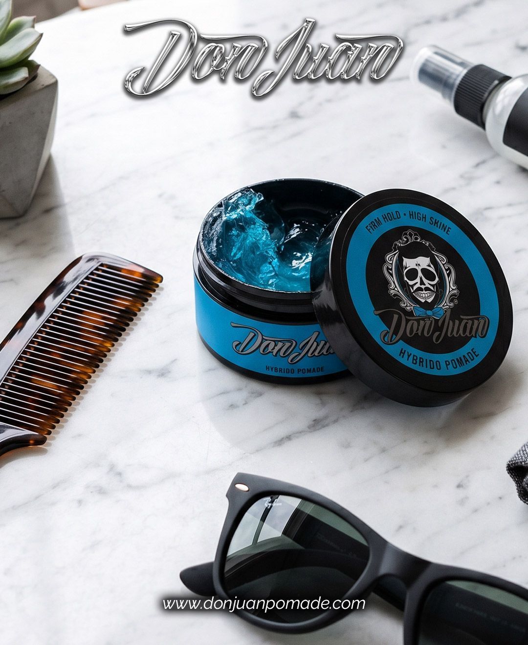 Una lata de pomada azul para el cabello y unas gafas de sol sobre una superficie de mármol, con un peine y una herramienta de barbero cerca.