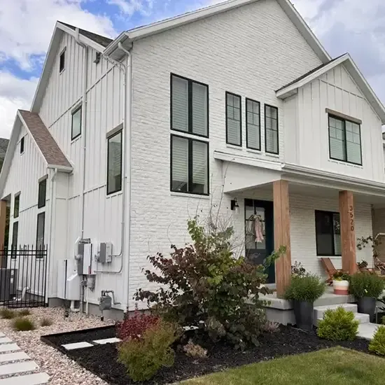 Radon mitigation system installed on a white modern farmhouse in Utah, with the vent pipe run flush against the siding and painted to blend in