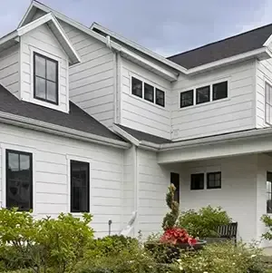 Radon mitigation system installed on a white modern farmhouse in Utah, with the vent pipe run flush against the siding and painted to blend in