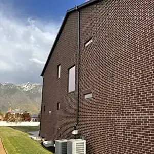 Radon mitigation system installed on a white modern farmhouse in Utah, with the vent pipe run flush against the siding and painted to blend in
