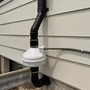 Radon mitigation system installed on a white modern farmhouse in Utah, with the vent pipe run flush against the siding and painted to blend in