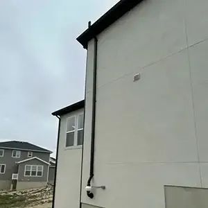 Radon mitigation system installed on a white modern farmhouse in Utah, with the vent pipe run flush against the siding and painted to blend in
