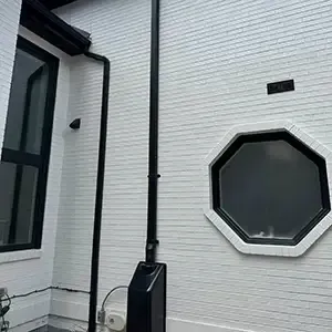 Radon mitigation system installed on a white modern farmhouse in Utah, with the vent pipe run flush against the siding and painted to blend in