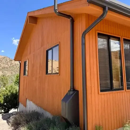 Radon mitigation system installed on a white modern farmhouse in Utah, with the vent pipe run flush against the siding and painted to blend in