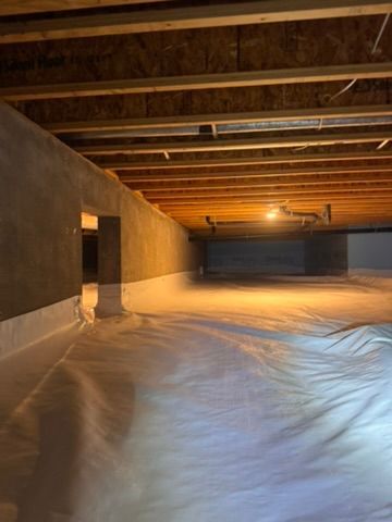 Unfinished basement with exposed beams, concrete walls, and a white tarp covering the floor.