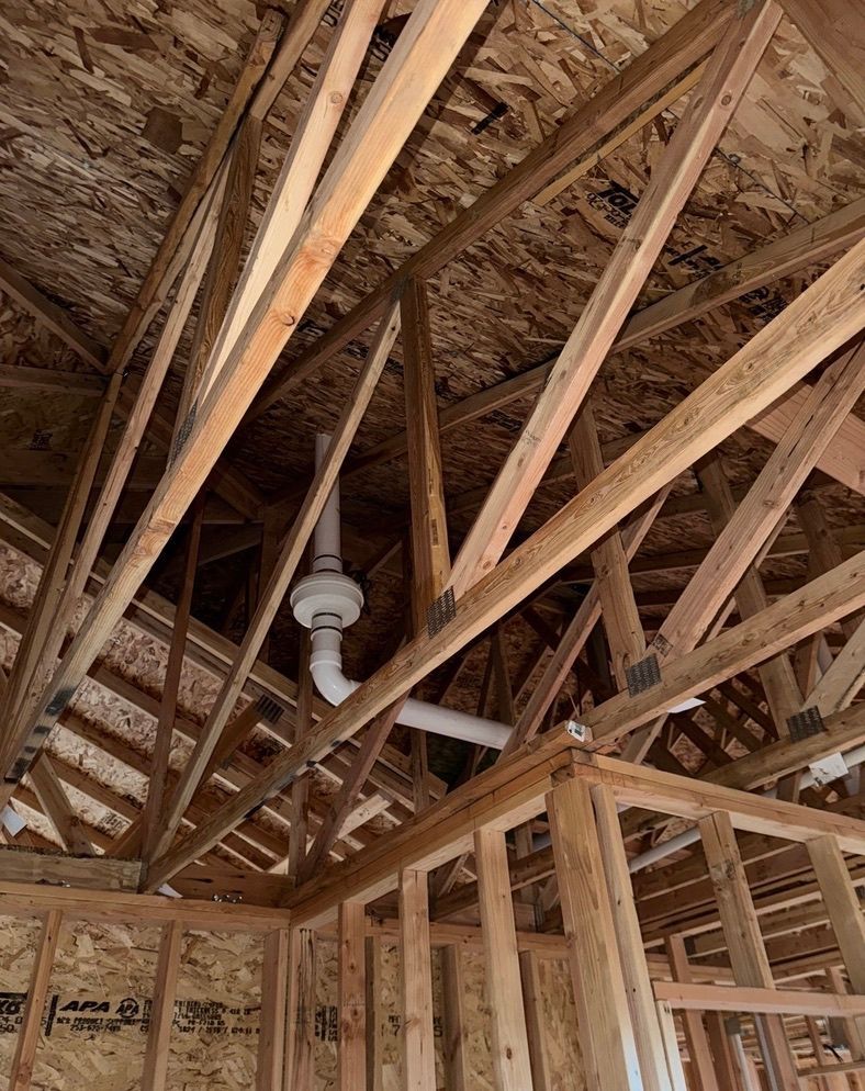 Exposed wooden roof framing in an unfinished house with a ceiling fan and visible rafters and trusses