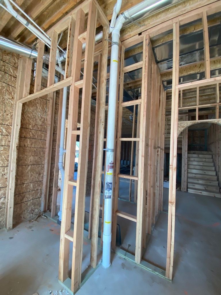 Interior of a framed house under construction with exposed wood studs and blue PVC pipes