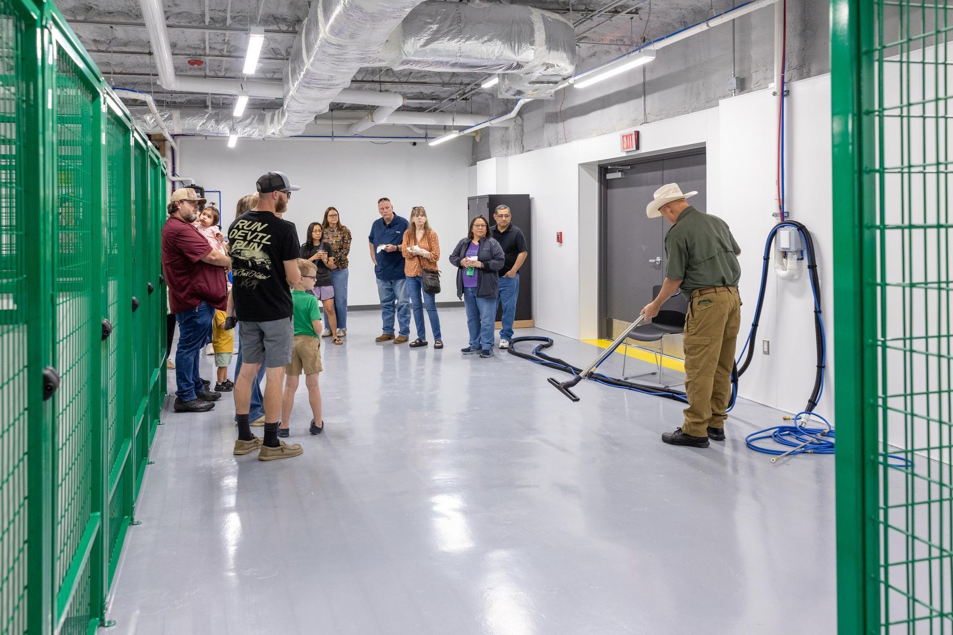 Group watches a man demonstrate with a hose in a modern, light-filled room with green cages.