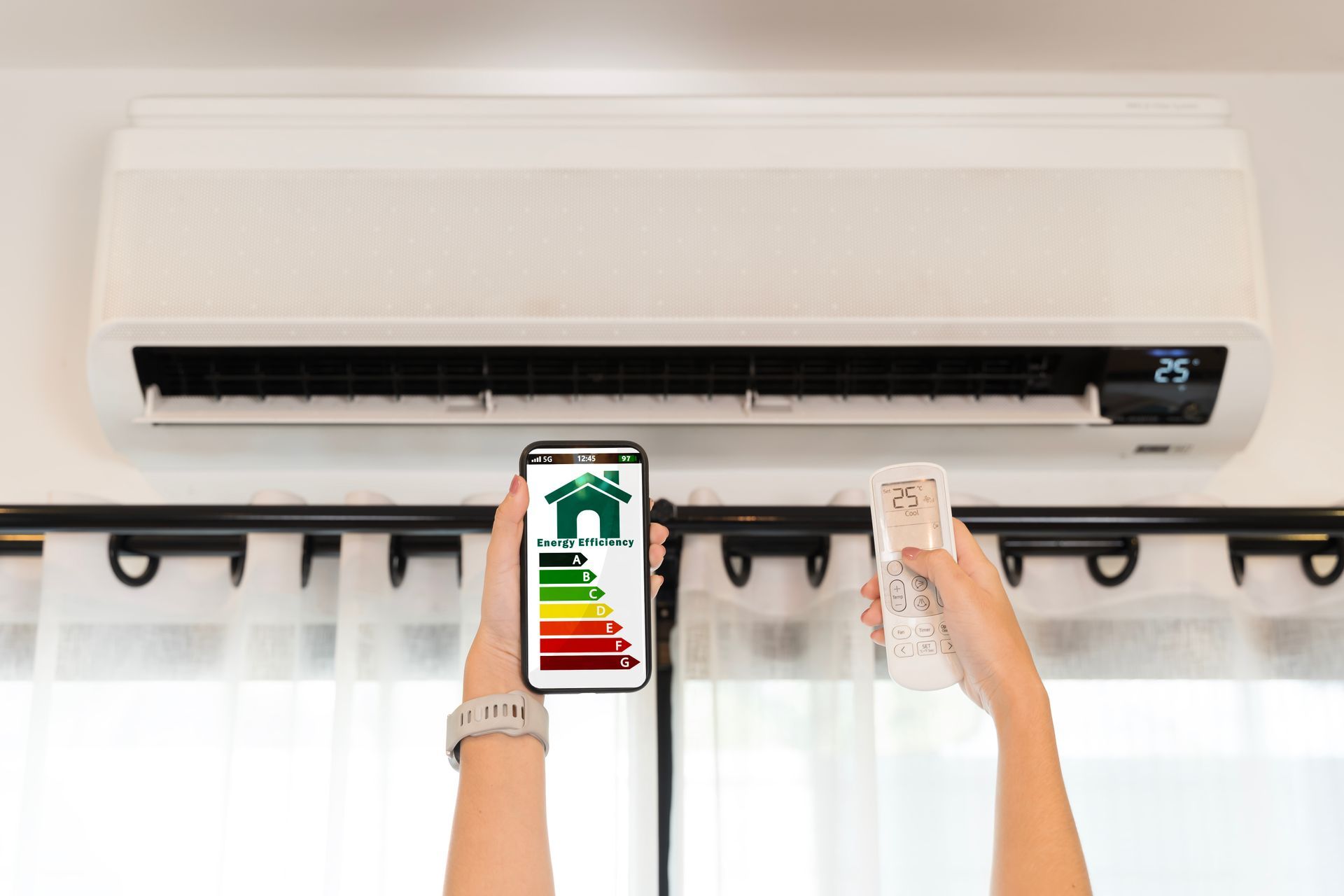 A pair of hands holding an air conditioner remote and smartphone with an energy-saving system.