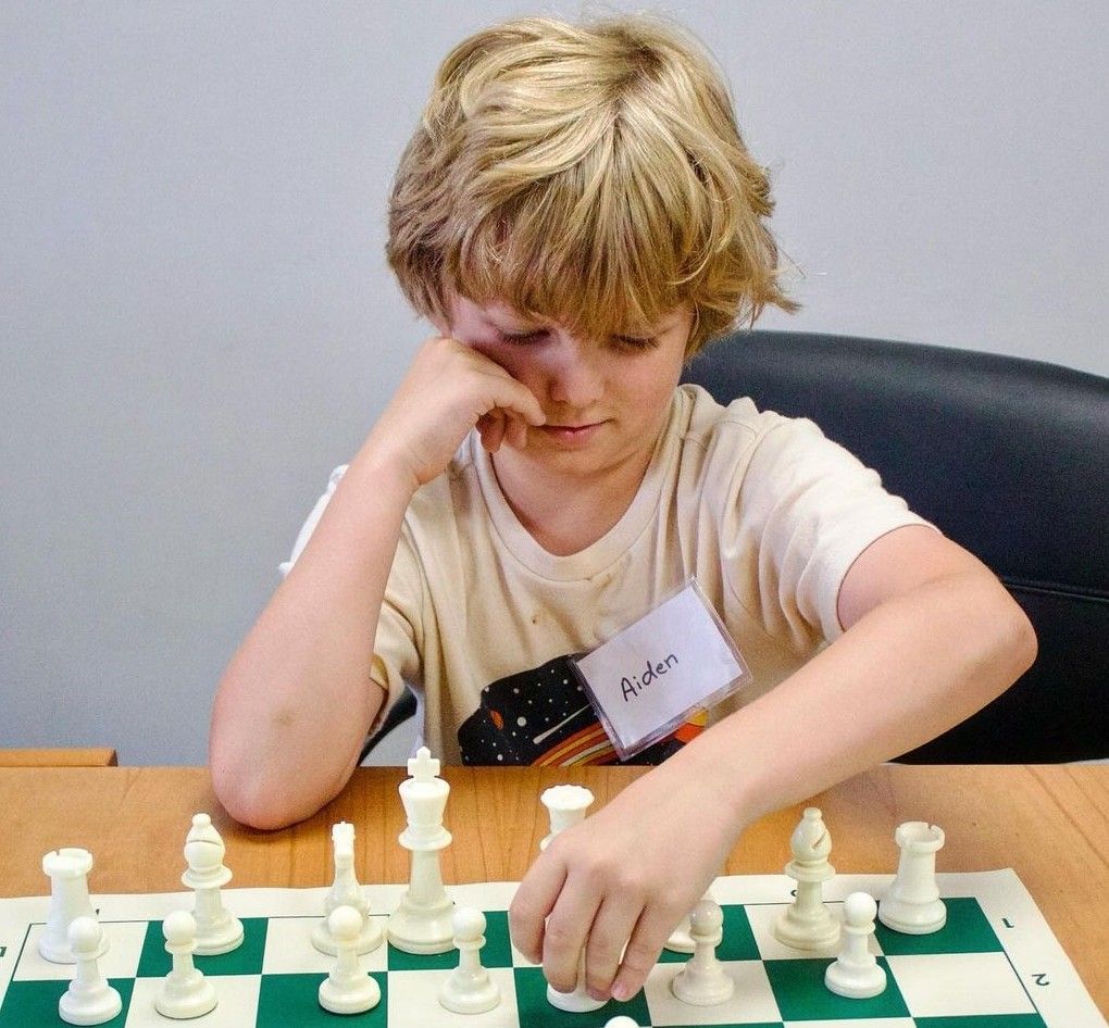 Child concentrating on a chess game, moving a white piece at a table.