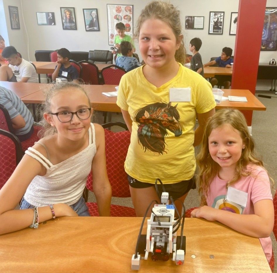 Three children at a table with a small robot in a restaurant or café setting.