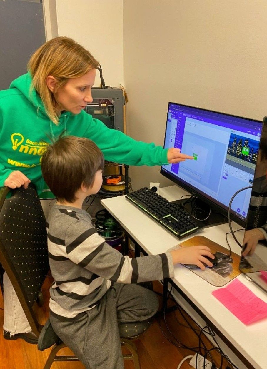 Adult helping child at desktop computer, pointing at the monitor in an office setting.
