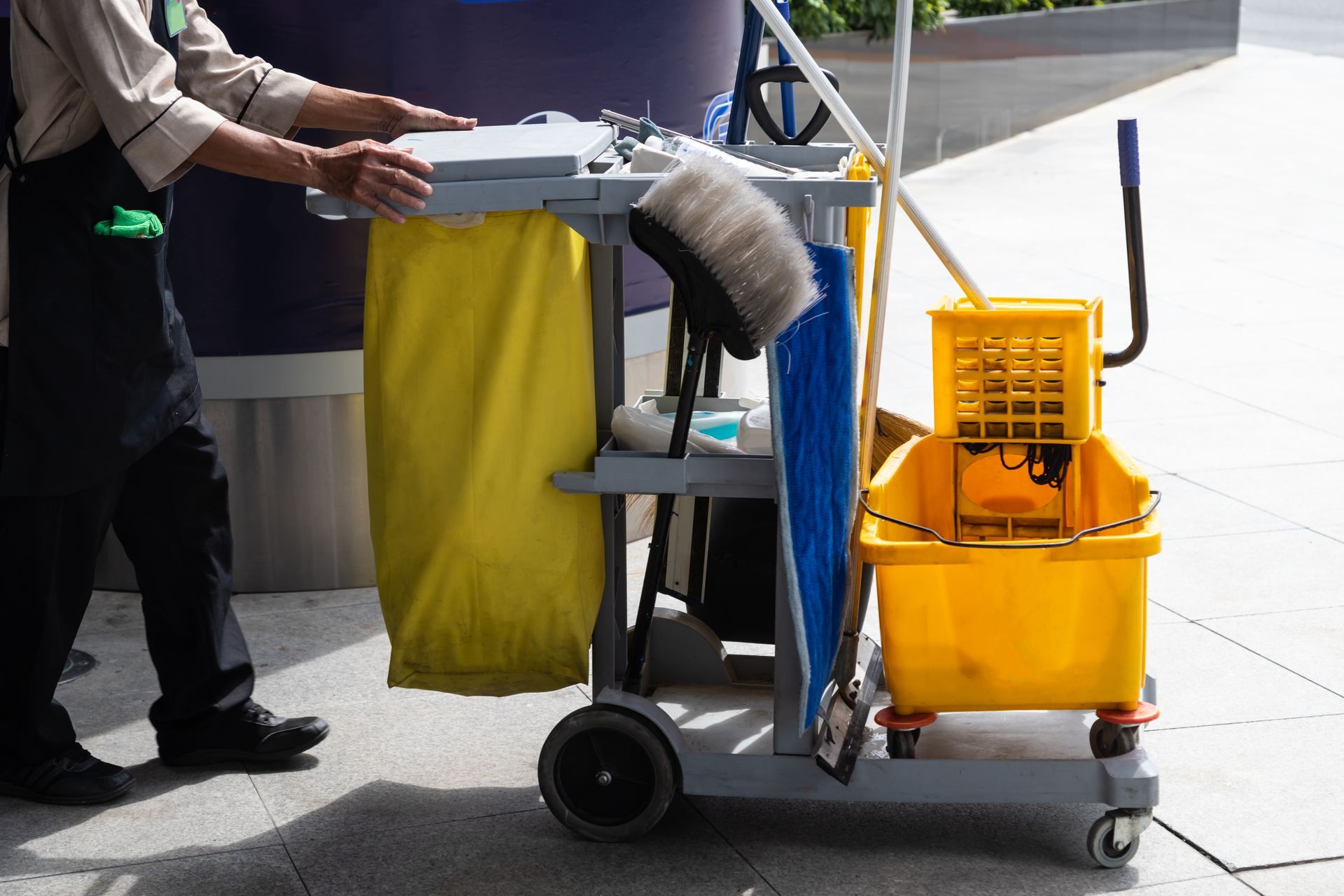 Janitor cart with mop, bucket, and cleaning supplies beside a person on a sidewalk