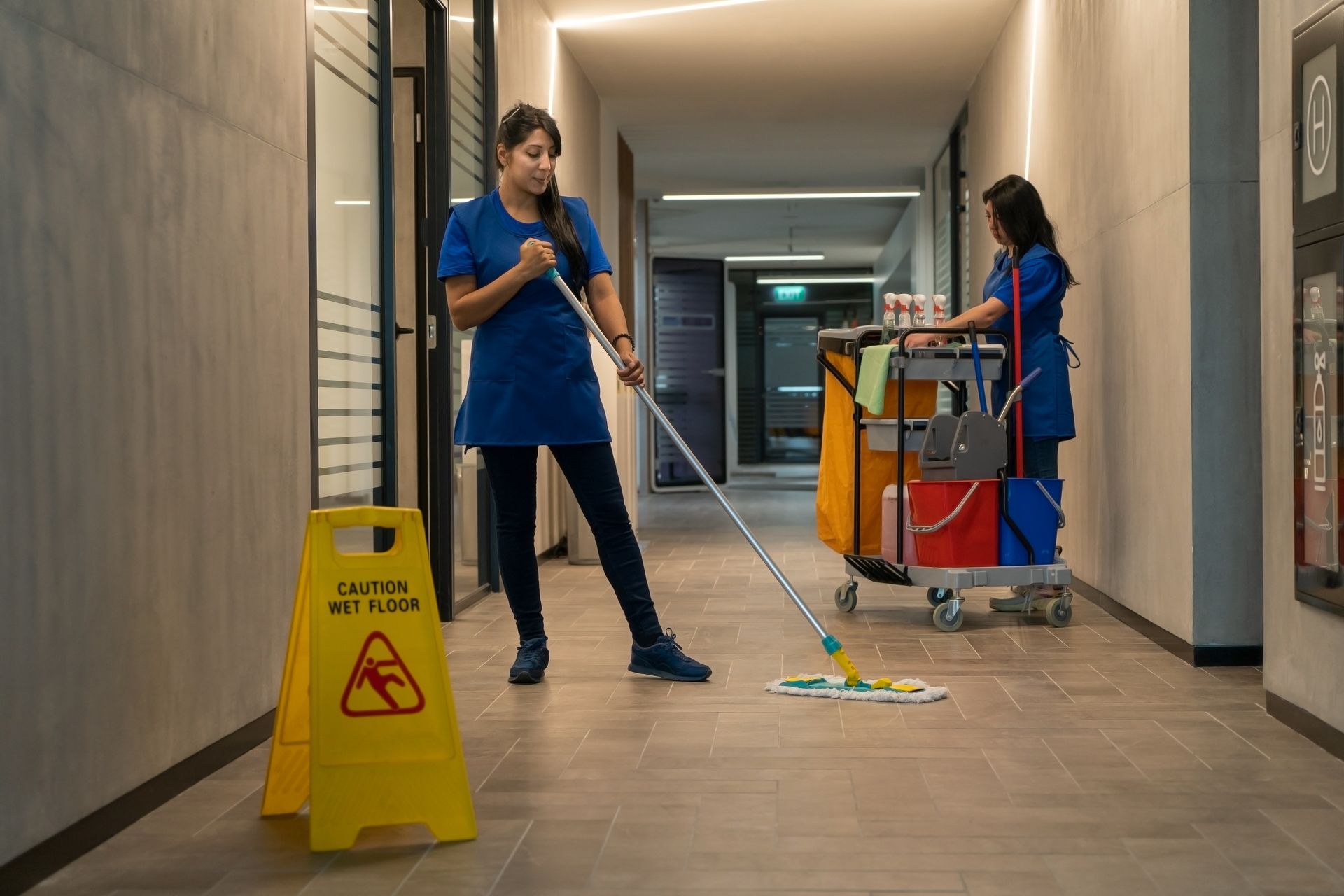 Two cleaners mopping a hallway.