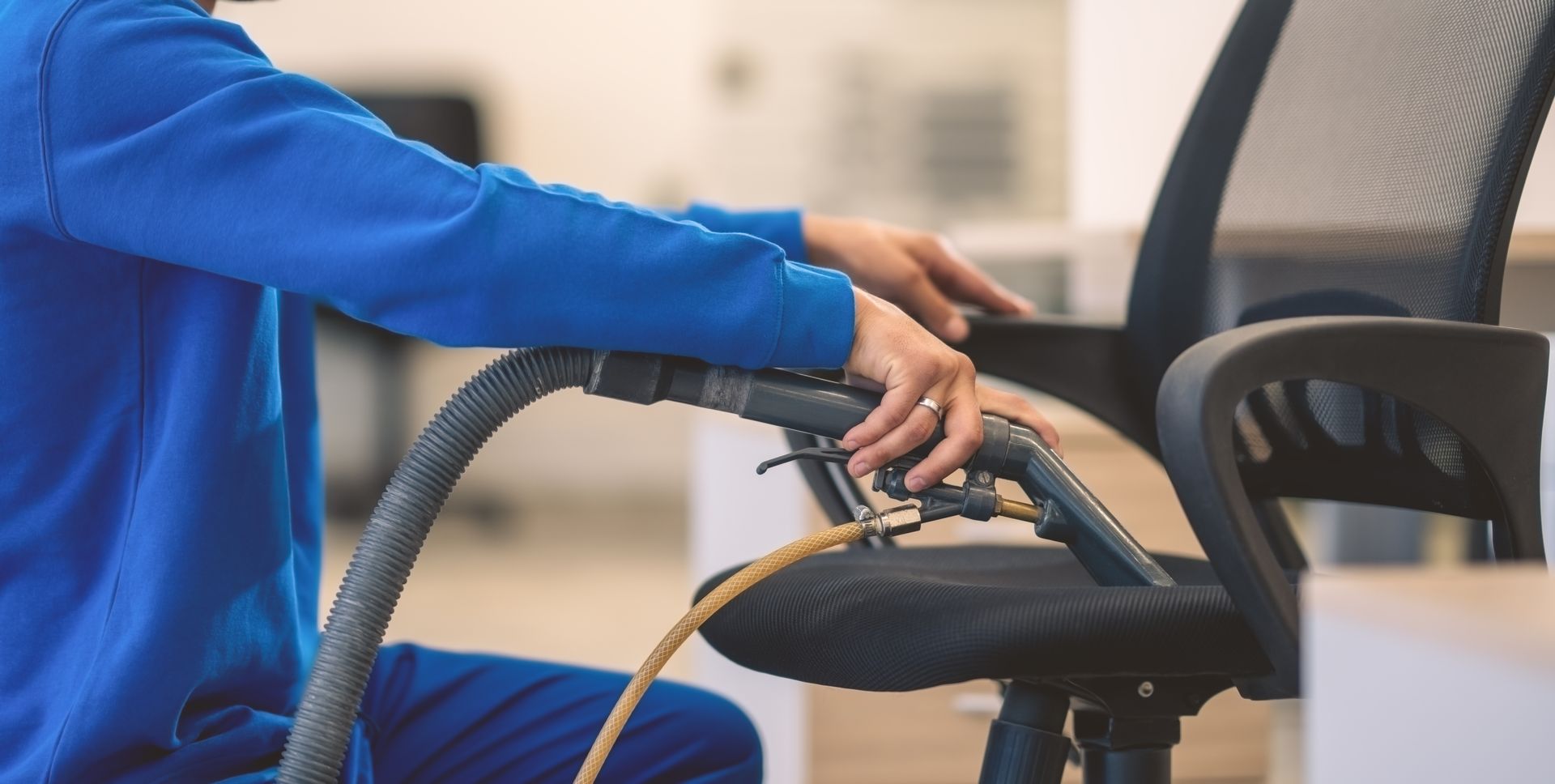 Person using a vacuum hose to clean a black office chair in an office setting