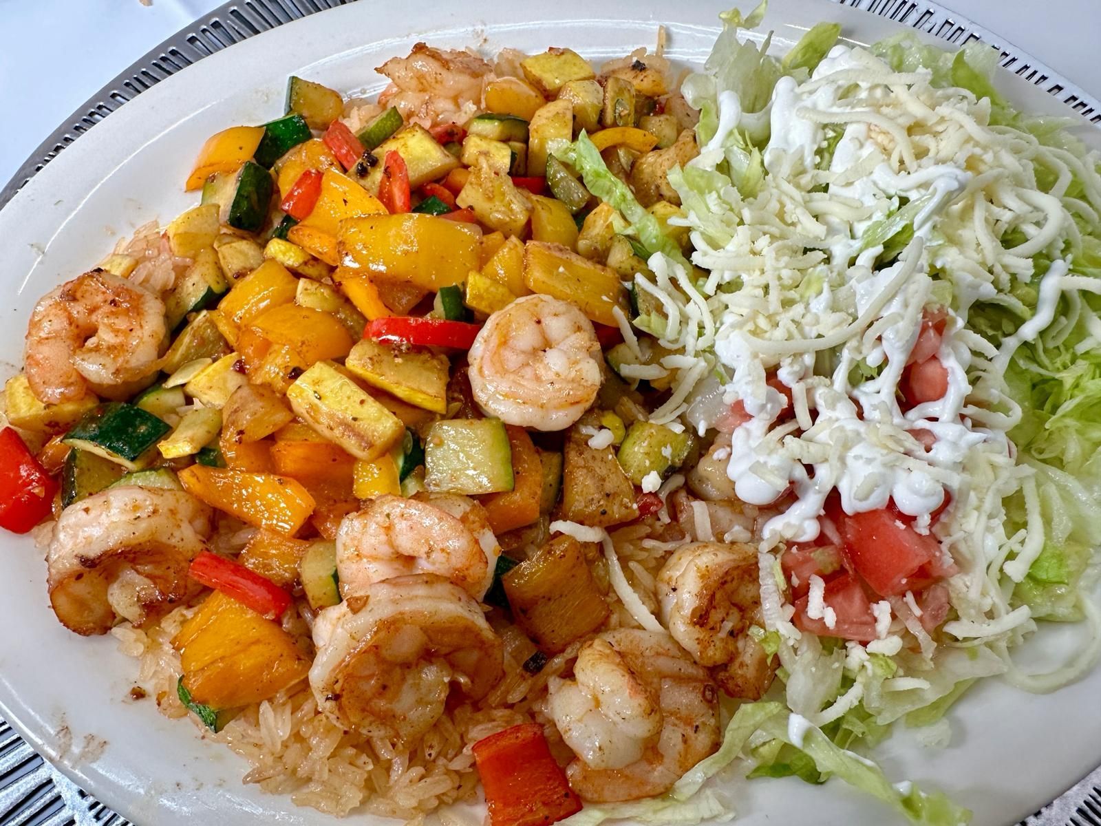 Plate of food with shrimp, vegetables, rice, and shredded lettuce with dressing.