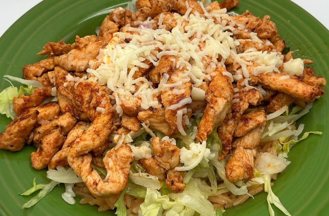 Chicken fajita salad with shredded cheese on a green plate.