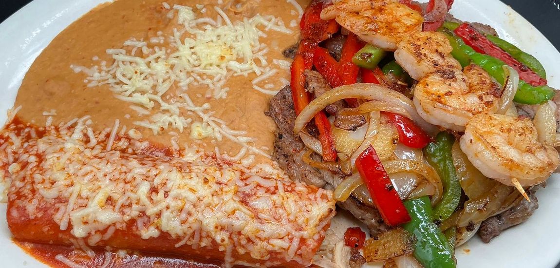 Plate of Mexican food: enchilada, refried beans, grilled peppers, onions, steak and shrimp.