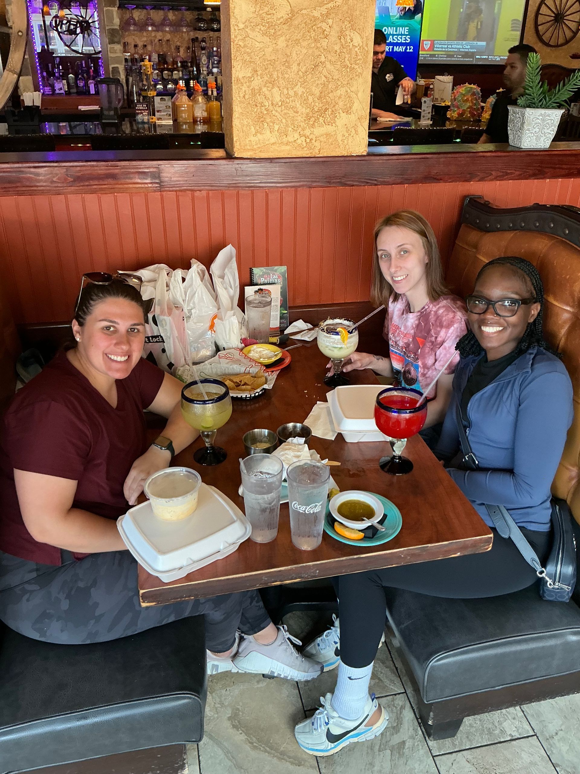 Three people at a restaurant table, smiling, with drinks and food.