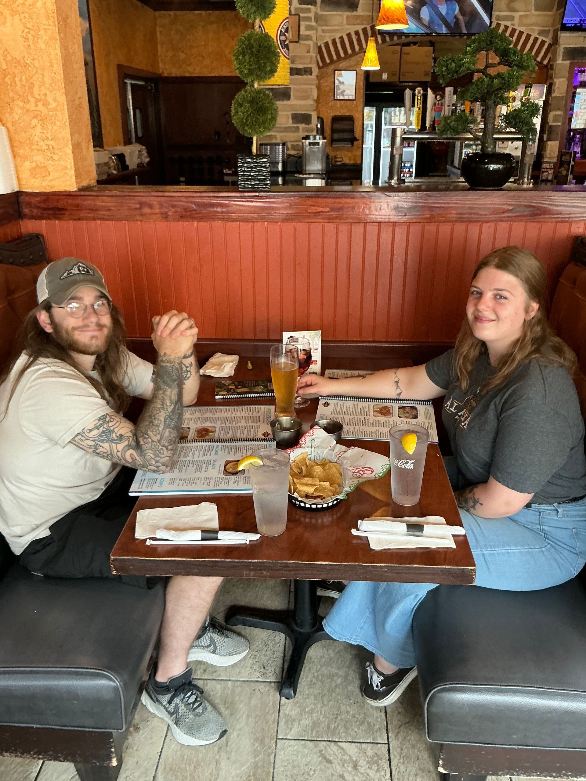 Two people seated at a table in a restaurant. They are smiling. There is food and drinks on the table.