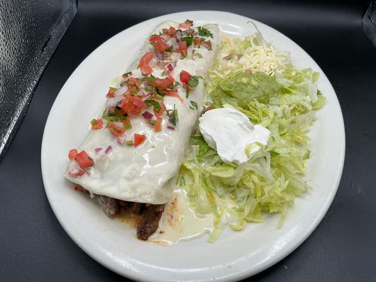 Burrito with white sauce and salsa, served with lettuce, guacamole, and sour cream on a white plate.