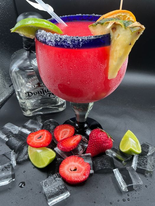 Strawberry margarita in a salt-rimmed glass, with tequila bottle, ice, limes, and strawberries.