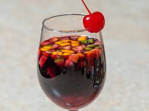 Sangria in a wine glass, garnished with a cherry and assorted diced fruit.