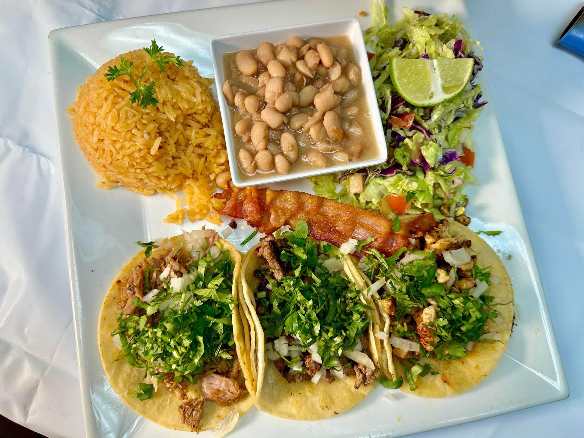 Plate with Mexican food: tacos, rice, beans, bacon, and salad.